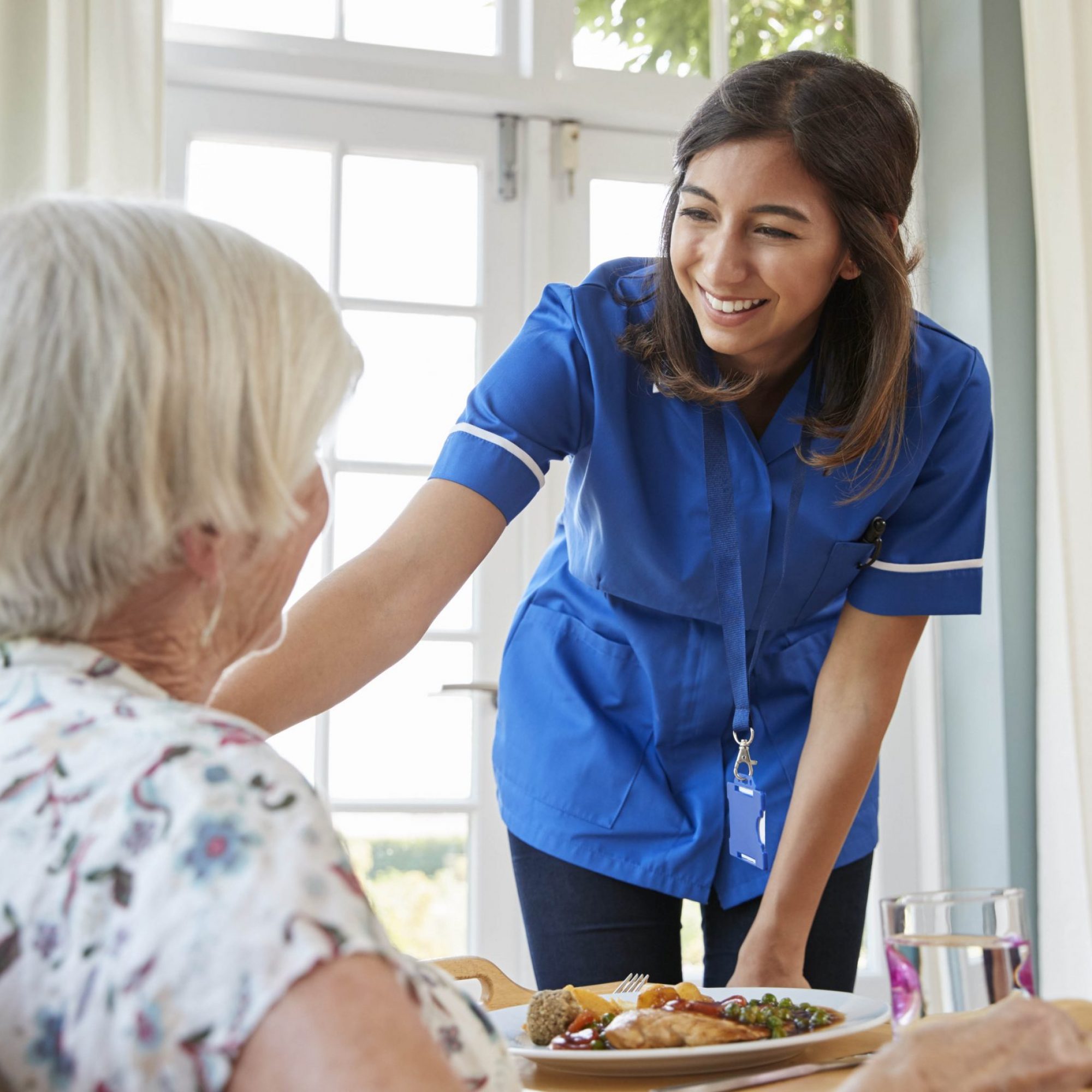 Care nurse serving dinner to a senior woman at home